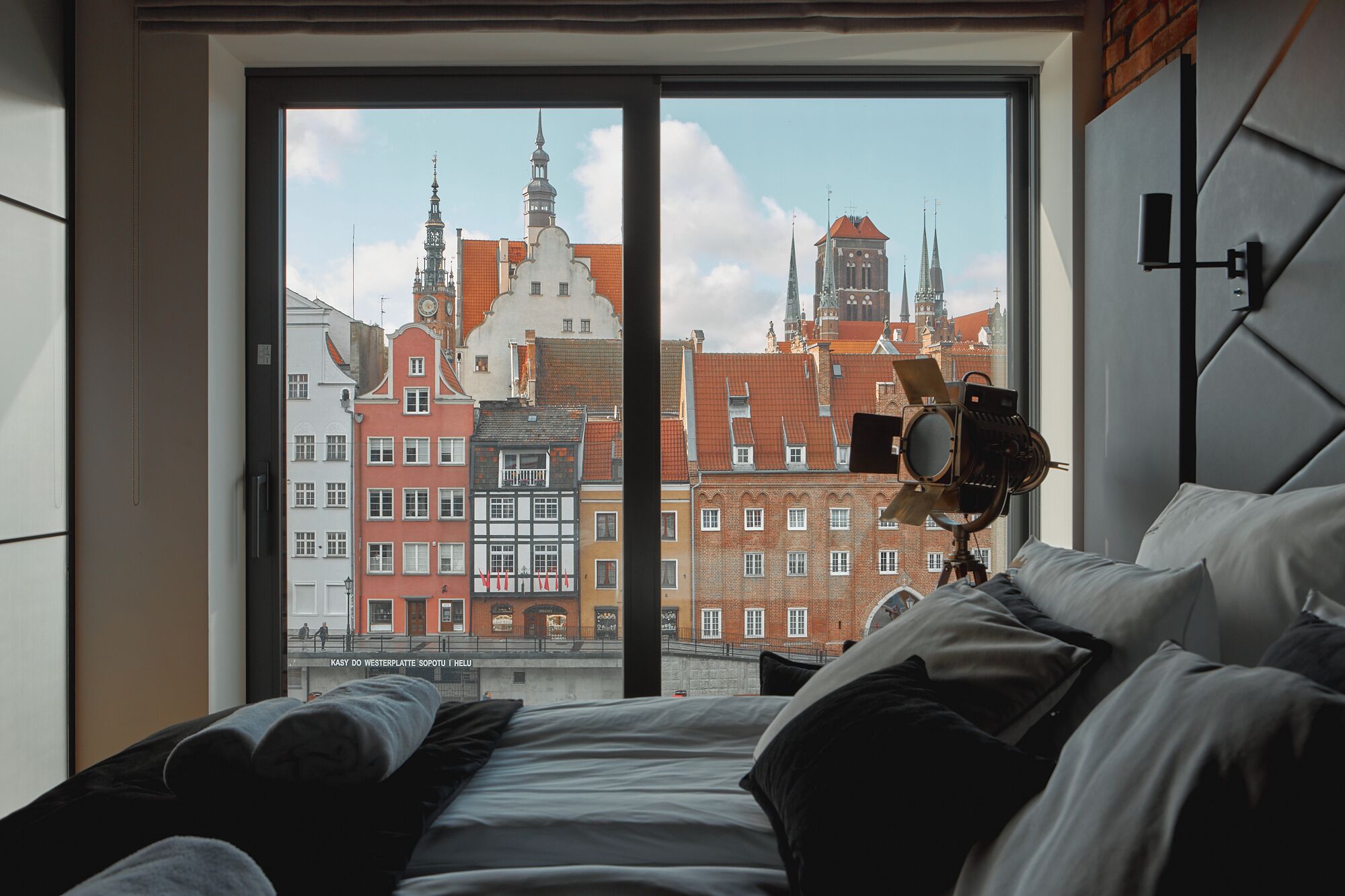 A hotel room with a large window overlooking historic buildings and a camera on a tripod.