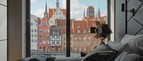 A hotel room with a large window overlooking historic buildings and a camera on a tripod.
