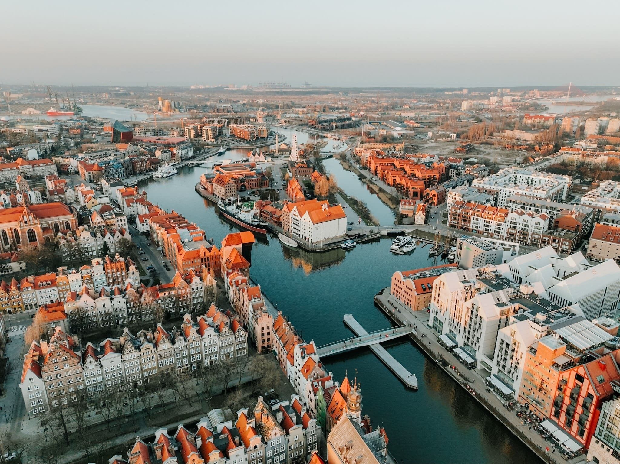 An aerial view of a city with a river running through it, featuring historic buildings with red roofs and modern structures.