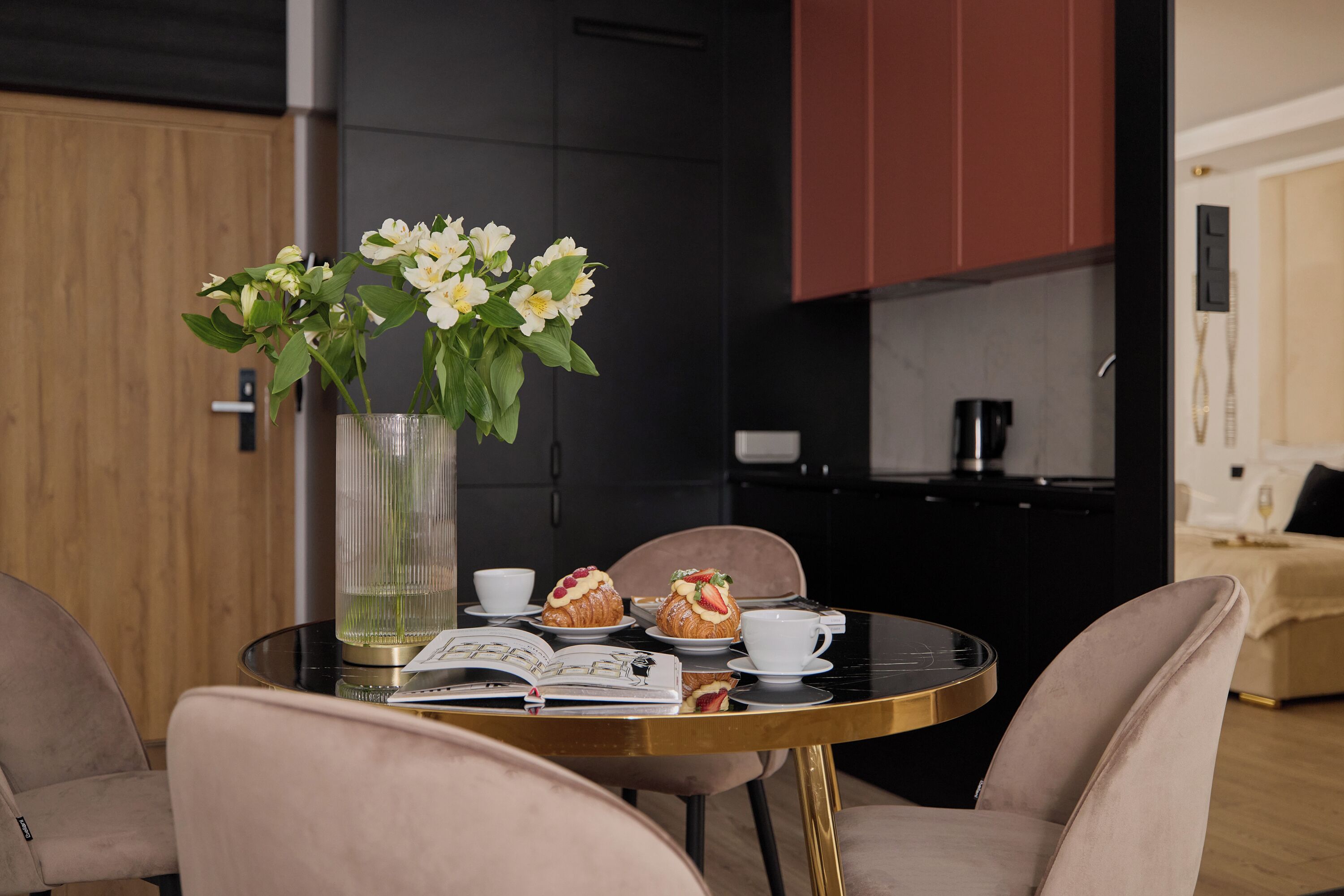 Una mesa de comedor con un florero, dos pasteles, una taza y un libro abierto.
