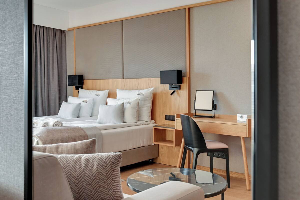 A hotel room with a bed, a desk, a chair, and a glass table.