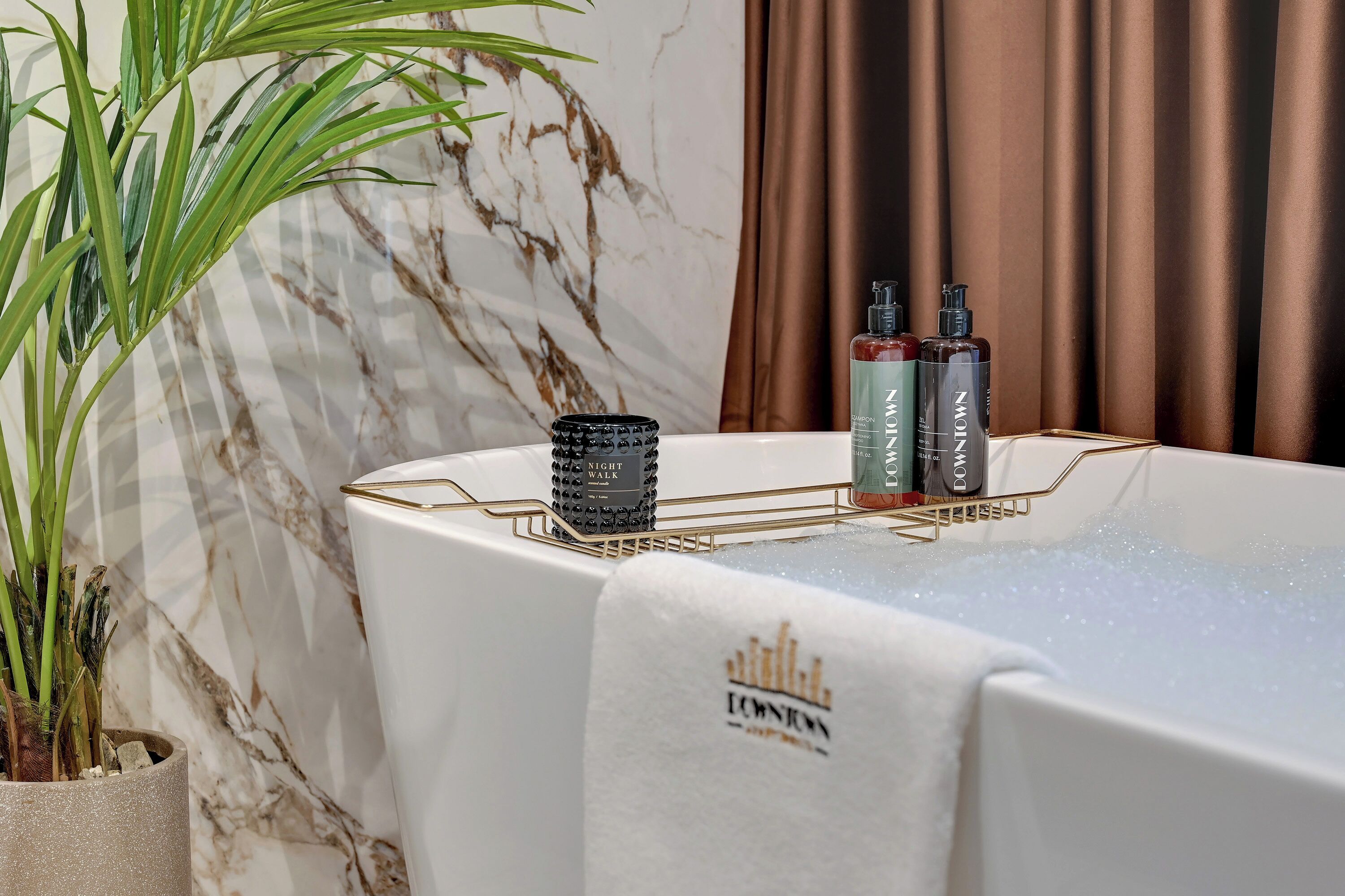 A spa area with a marble wall, a plant, a towel, and two bottles of Downy products on a tray.