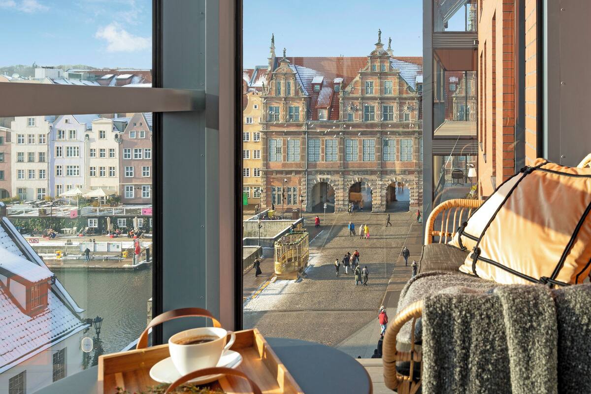 A view from a room with a large window overlooking a historic building and a canal.