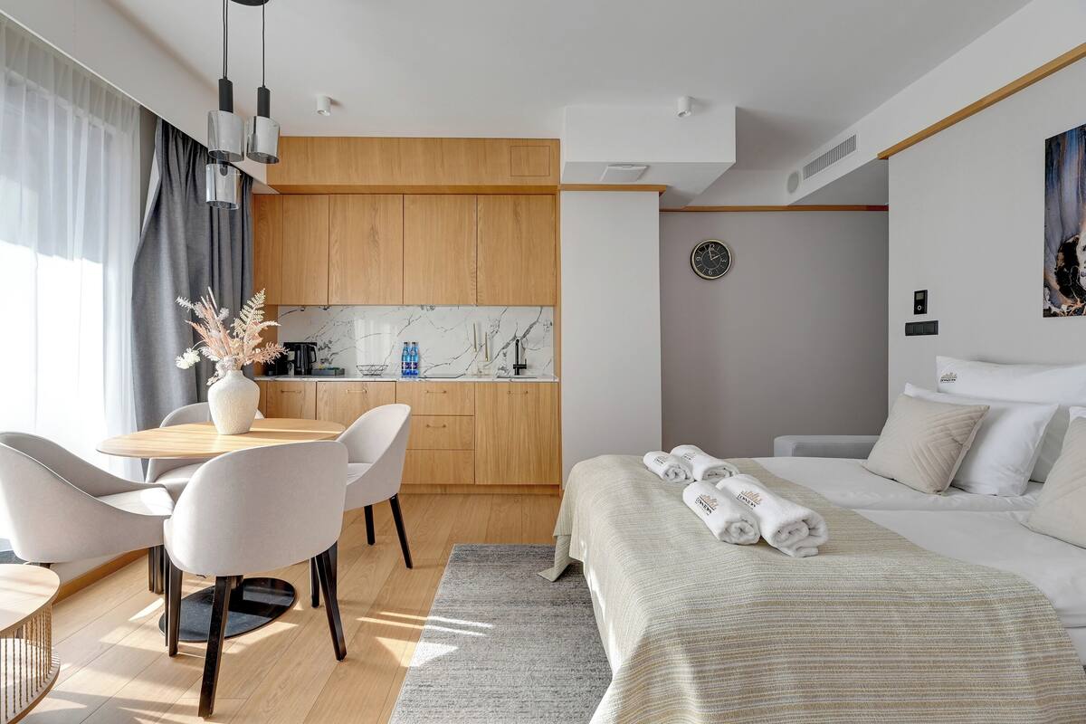 A modern hotel room with a wooden dining area, a bed with neatly folded towels, and a view of the city.