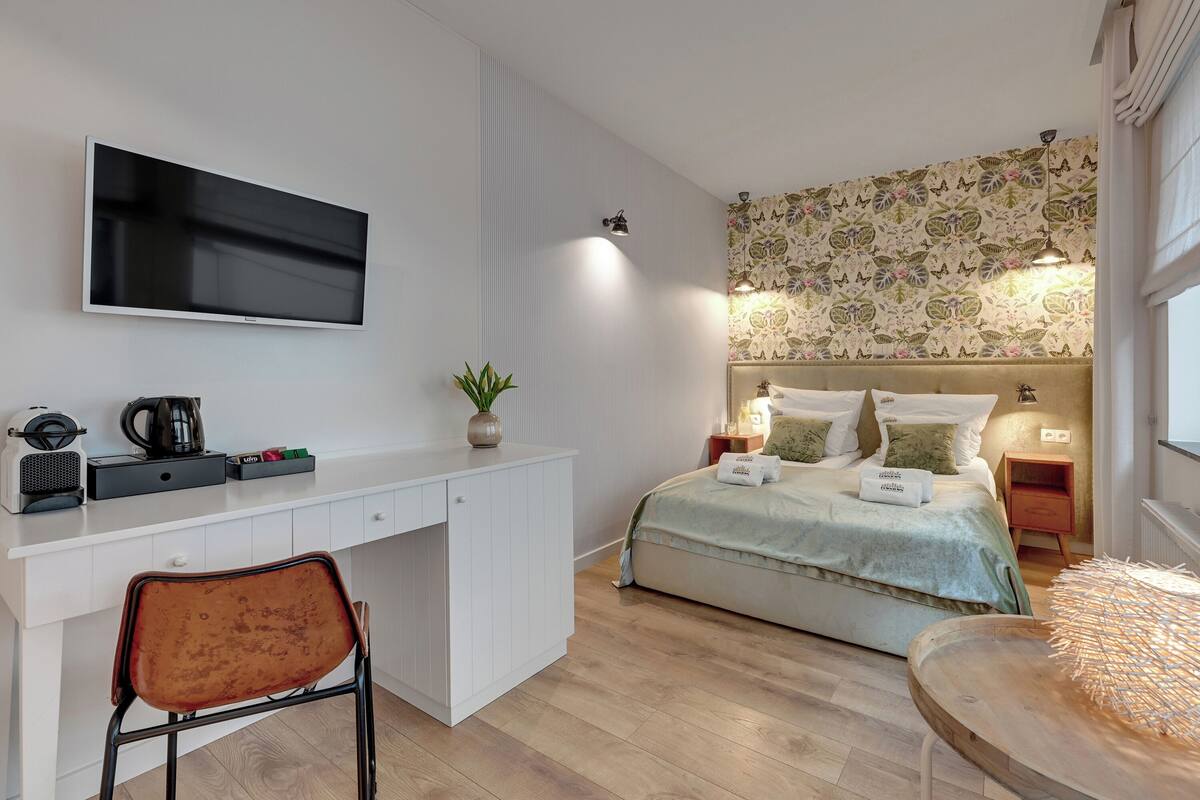 A modern bedroom with a bed, bedside tables, a desk, a chair, a TV, and a patterned wallpaper.
