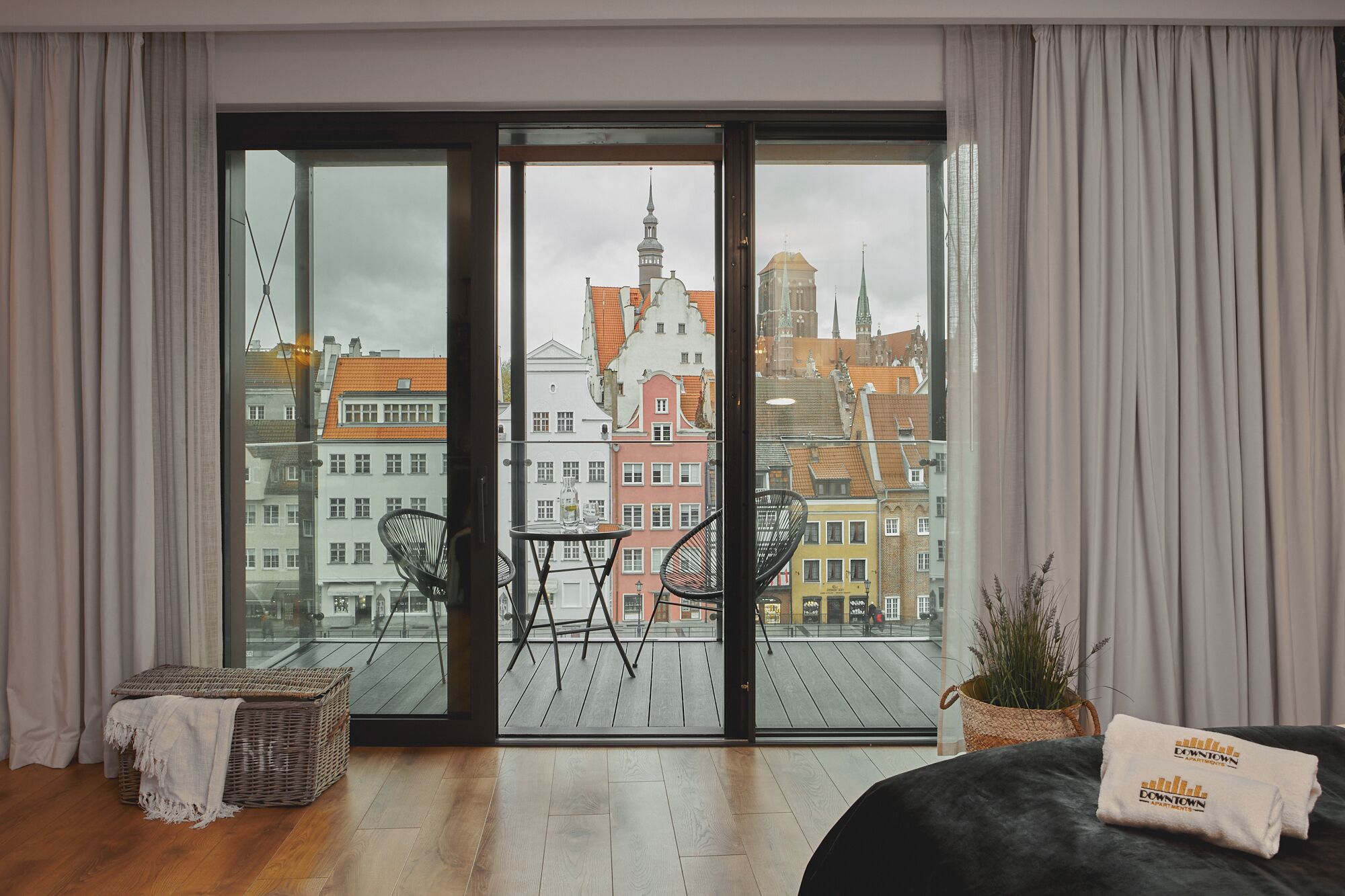 A modern apartment with a large sliding glass door leading to a balcony, offering a view of historic buildings and a church spire.