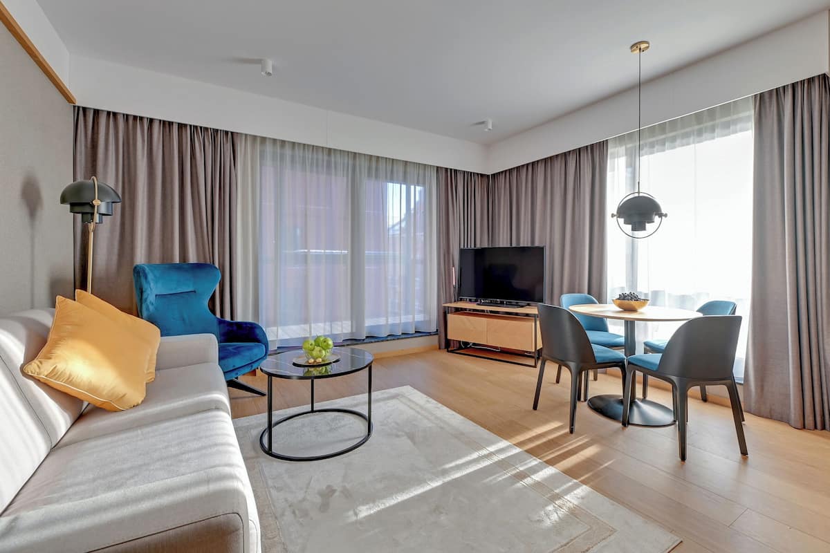 A modern living room with a sofa, a blue armchair, a coffee table, a TV, and a dining area with chairs and a table.