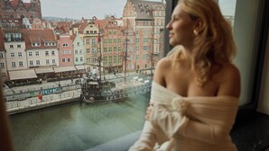A view of a historic cityscape with a river and a boat, and a person seated by a window. - Deo Plaza by Downtown Apartments (Gdansk)