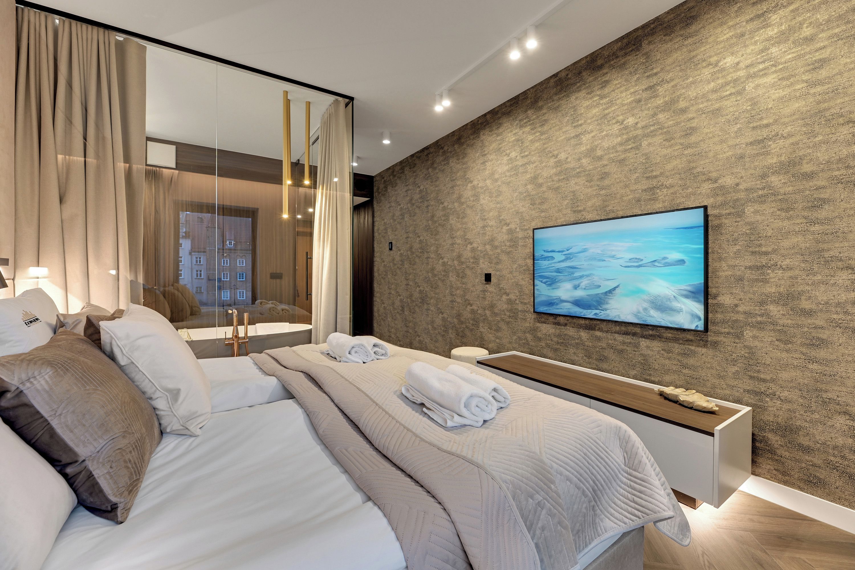 A modern hotel room with a large bed, a bedside table, a TV mounted on the wall, and a view of the city through the window.