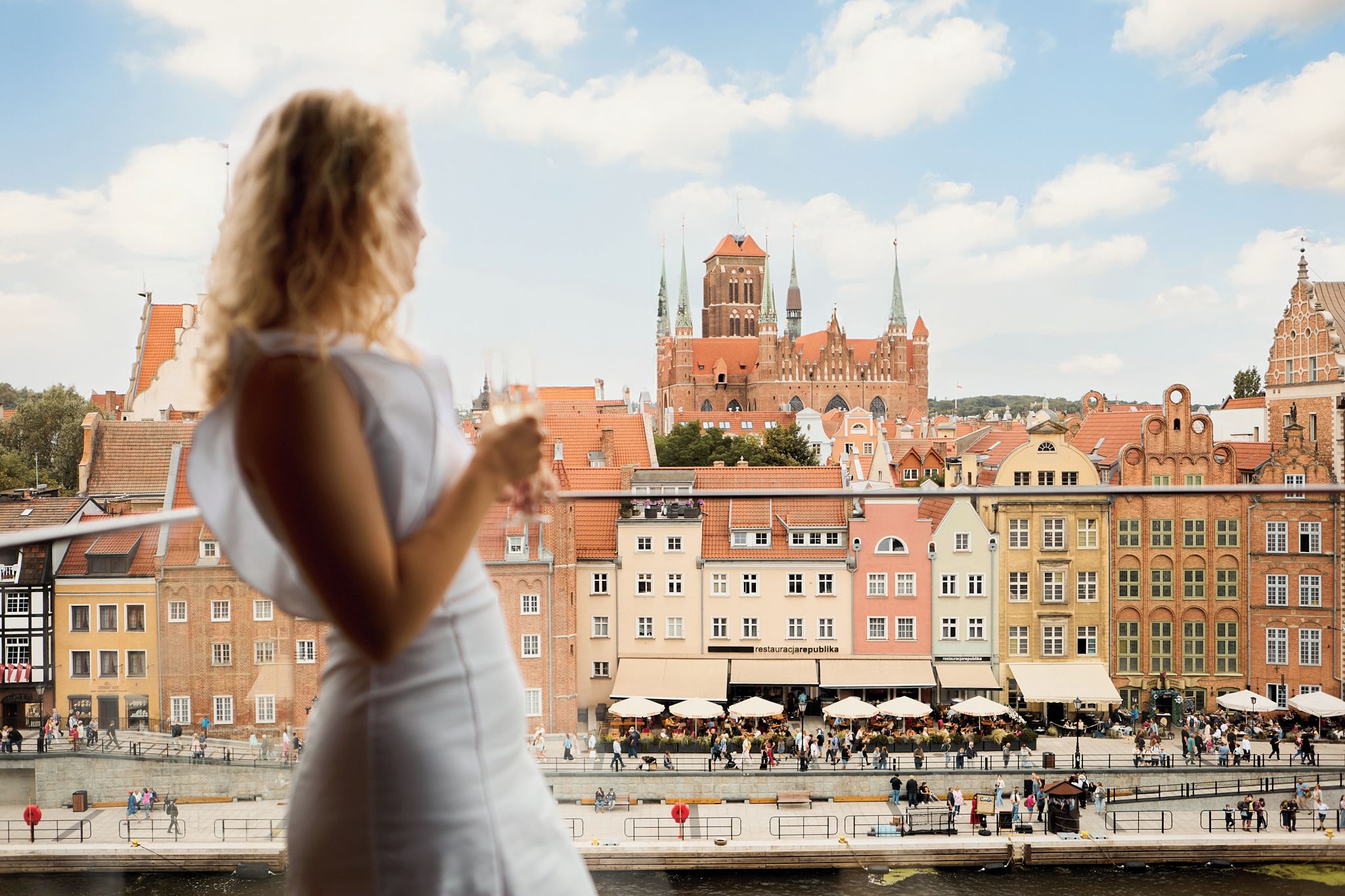 Eine Person blickt auf einen Fluss mit historischen Gebäuden und einer markanten Kirche im Hintergrund.