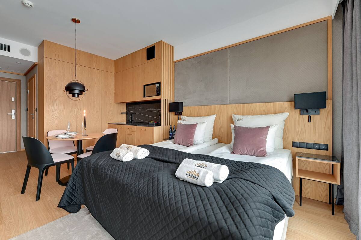 A modern hotel room with a large bed, a desk, and a kitchenette.