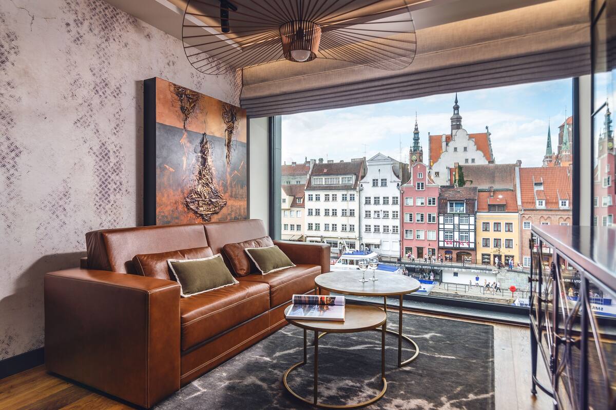 A modern living room with a leather sofa, a round coffee table, and a large window offering a view of historic buildings.