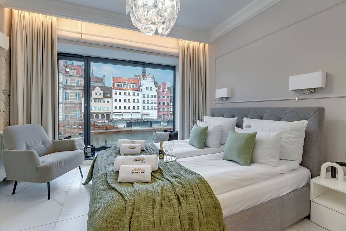 A modern hotel room with a large bed, a chair, and a view of a cityscape.