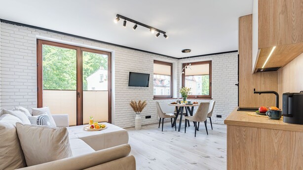 A modern kitchen with a wooden countertop, a dining area with a table and chairs, and a living room with a sofa and a TV mounted on the wall. - Imperial Apartments - Mewa (Sopot)
