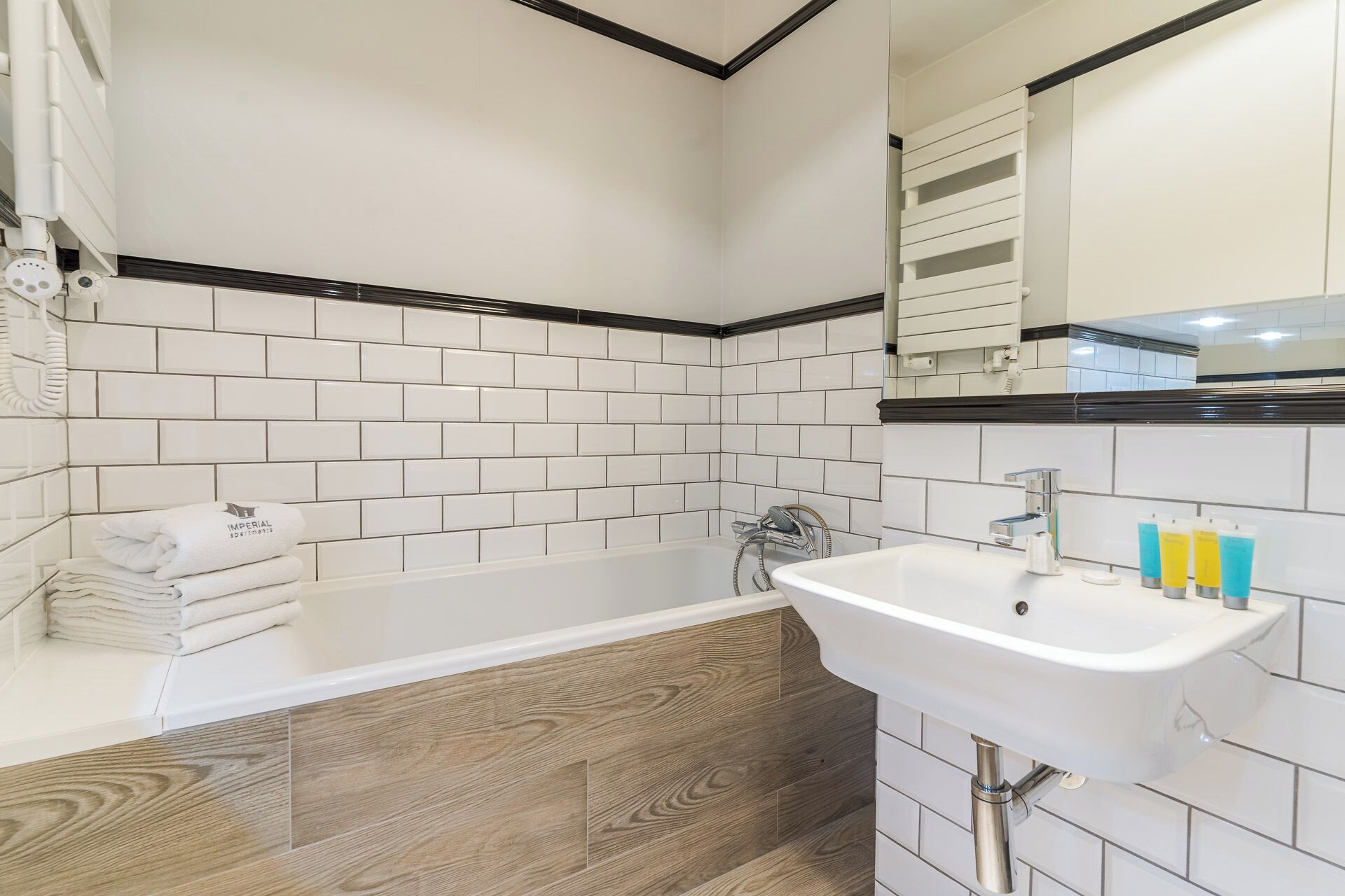 A bathroom with white subway tiles, a wooden vanity, a white sink, and a bathtub.