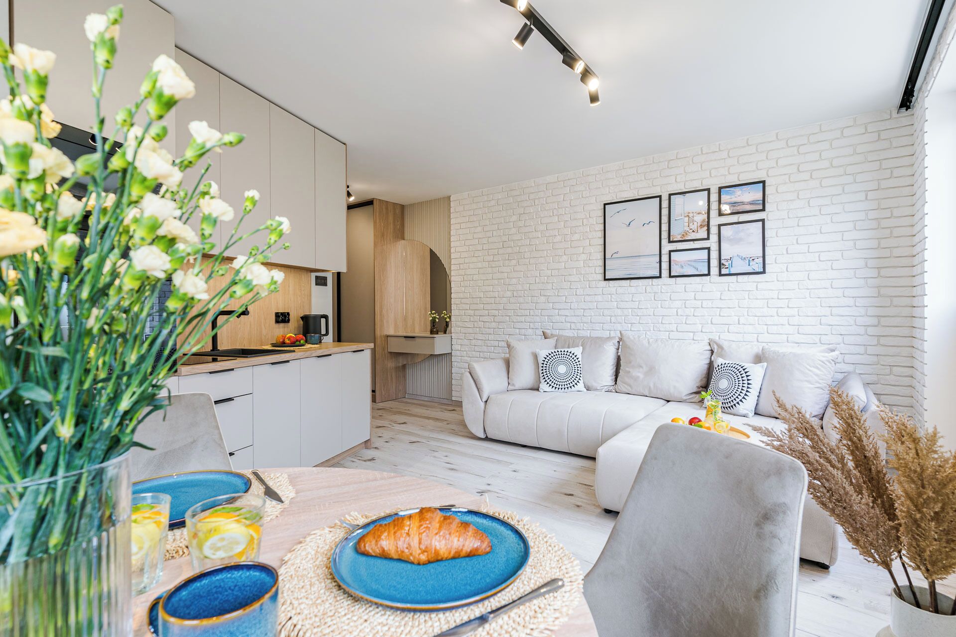 A modern living room with a white brick wall, a sofa, and a dining area with a table set for breakfast.