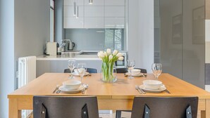 A modern dining area with a wooden table set for four, white plates, and clear glassware. A vase with white tulips is centered on the table. - Imperial Apartments - Mewa (Sopot)
