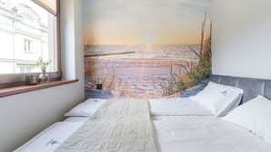 A bedroom with a bed, pillows, a window, and a wall mural of a beach scene. - Imperial Apartments - Mewa (Sopot)