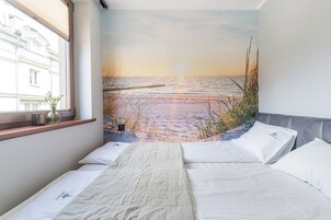 A bedroom with a bed, pillows, a window, and a wall mural of a beach scene.