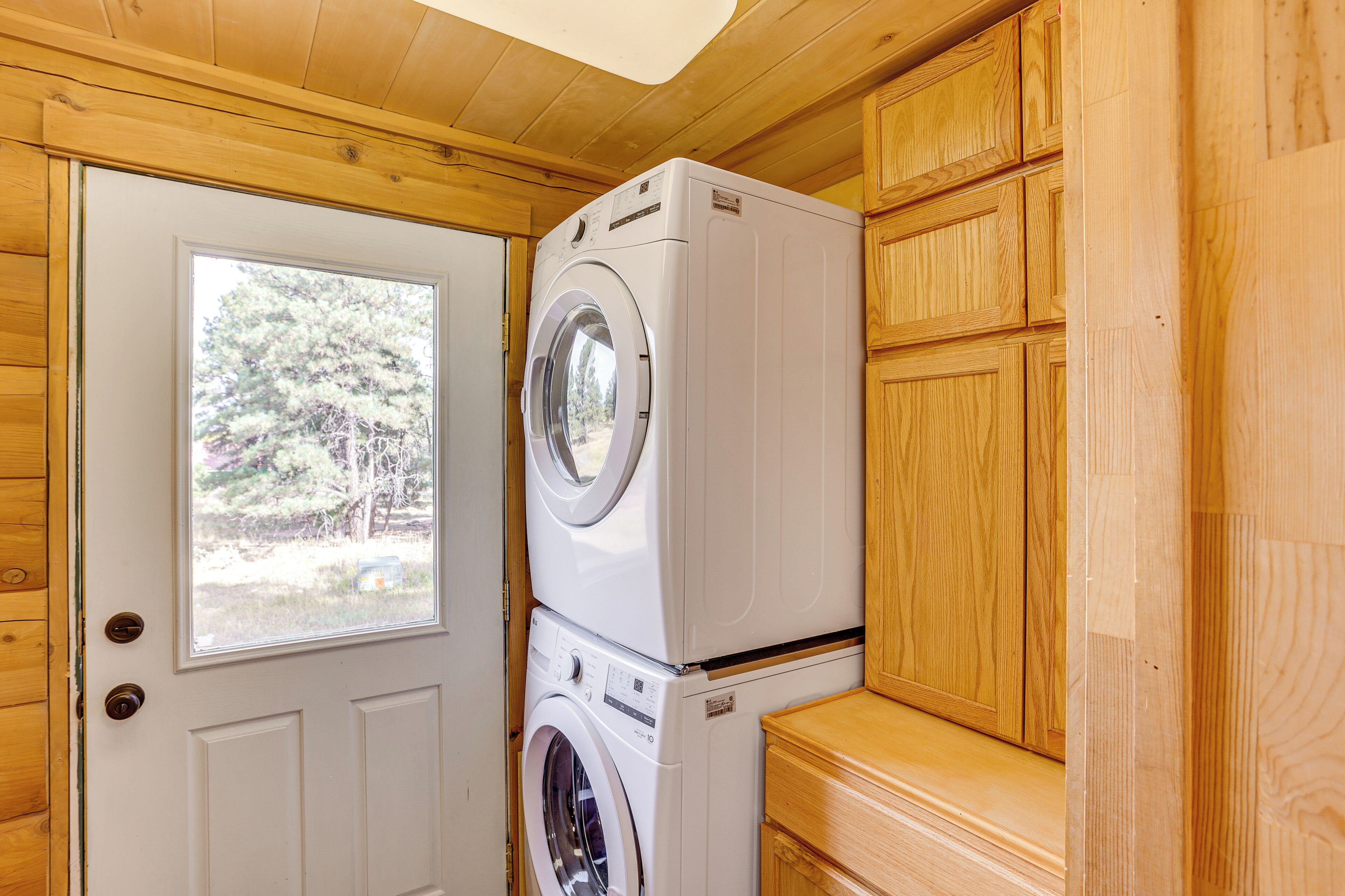 A compact laundry area with a front-loading washer and dryer, wooden cabinetry, and a window providing a view of the outdoors.