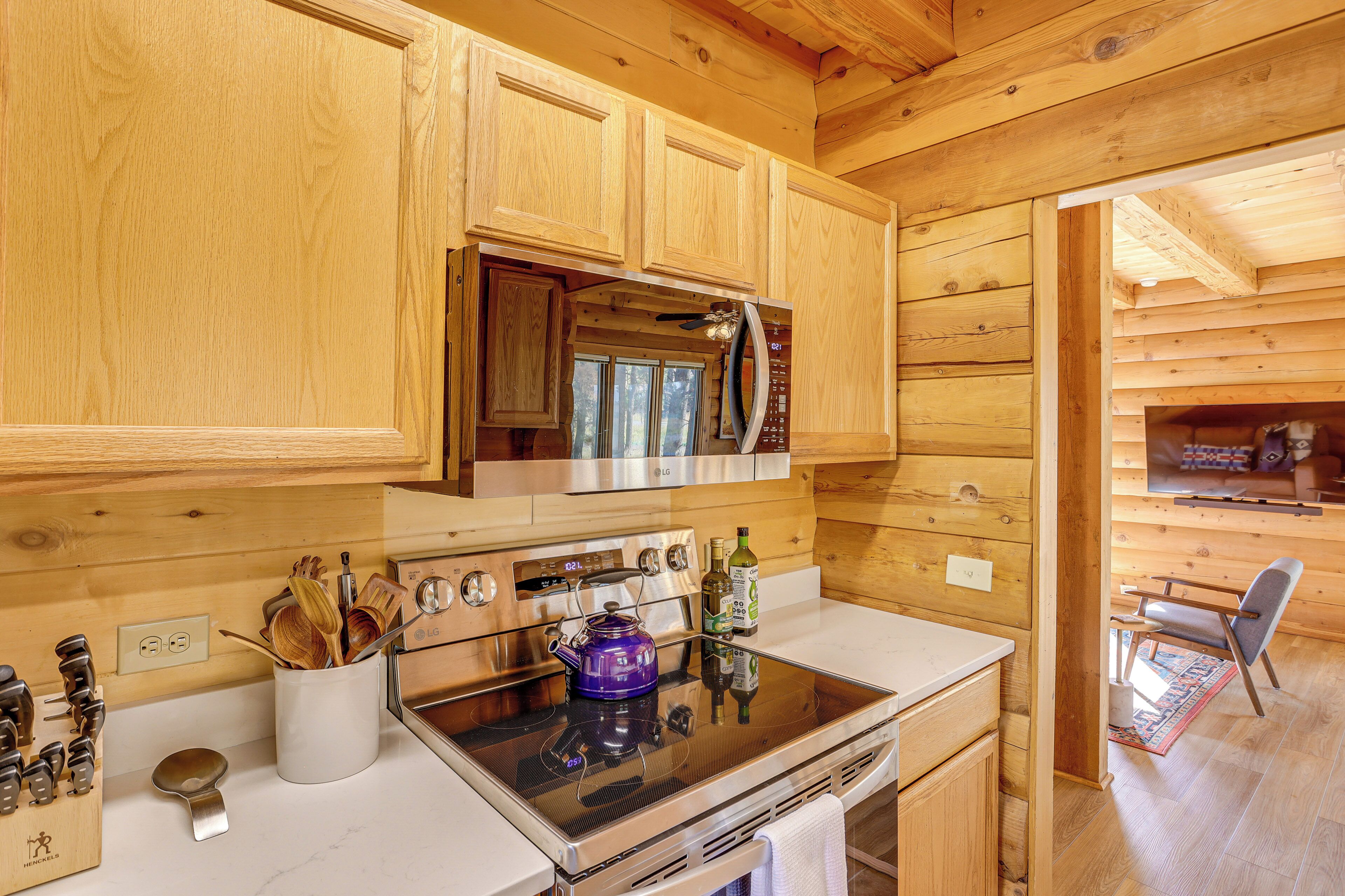 A kitchen with wooden cabinets, a stainless steel stove, and a microwave. There is a wooden cutting board and a knife block on the counter.