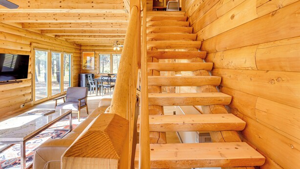 Ein Holzblockhaus-Interieur mit Treppe, Essbereich und Fernseher.