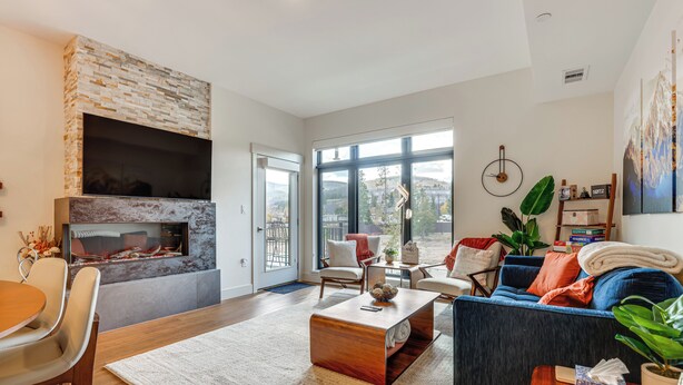A modern living room with a fireplace, comfortable seating, and large windows offering a view of the outdoors. - Mountain-view Condo in Downtown Winter Park! (Winter Park)