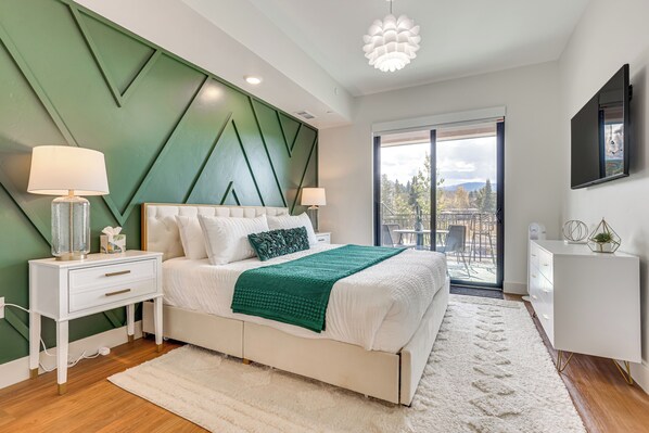 A modern bedroom with a bed, nightstands, a dresser, and a large window offering a view of the outdoors.