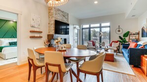 A modern living room with a dining area, featuring a fireplace, large windows, and a cozy seating arrangement. - Mountain-view Condo in Downtown Winter Park! (Winter Park)