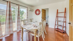 A dining area with a table set for four, a wooden chair, a red decorative wall piece, and a wooden ladder shelf.