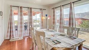 A dining area with a table set for two, curtains, and a view of the outdoors.