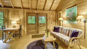 A wooden cabin interior with a dining table, chairs, a sofa, and a map on the wall. - Rustic Cabin w/ Squam Lake Access & Fireplace! (Holderness)