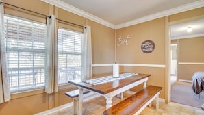 A dining area with a wooden table and benches, beige walls, and a window with blinds. - Lake-view Getaway w/ Grill in Mountain Home! (Mountain Home)