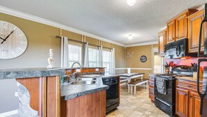 A kitchen with a large clock, wooden cabinets, a dishwasher, a stove, and a microwave. - Lake-view Getaway w/ Grill in Mountain Home! (Mountain Home)