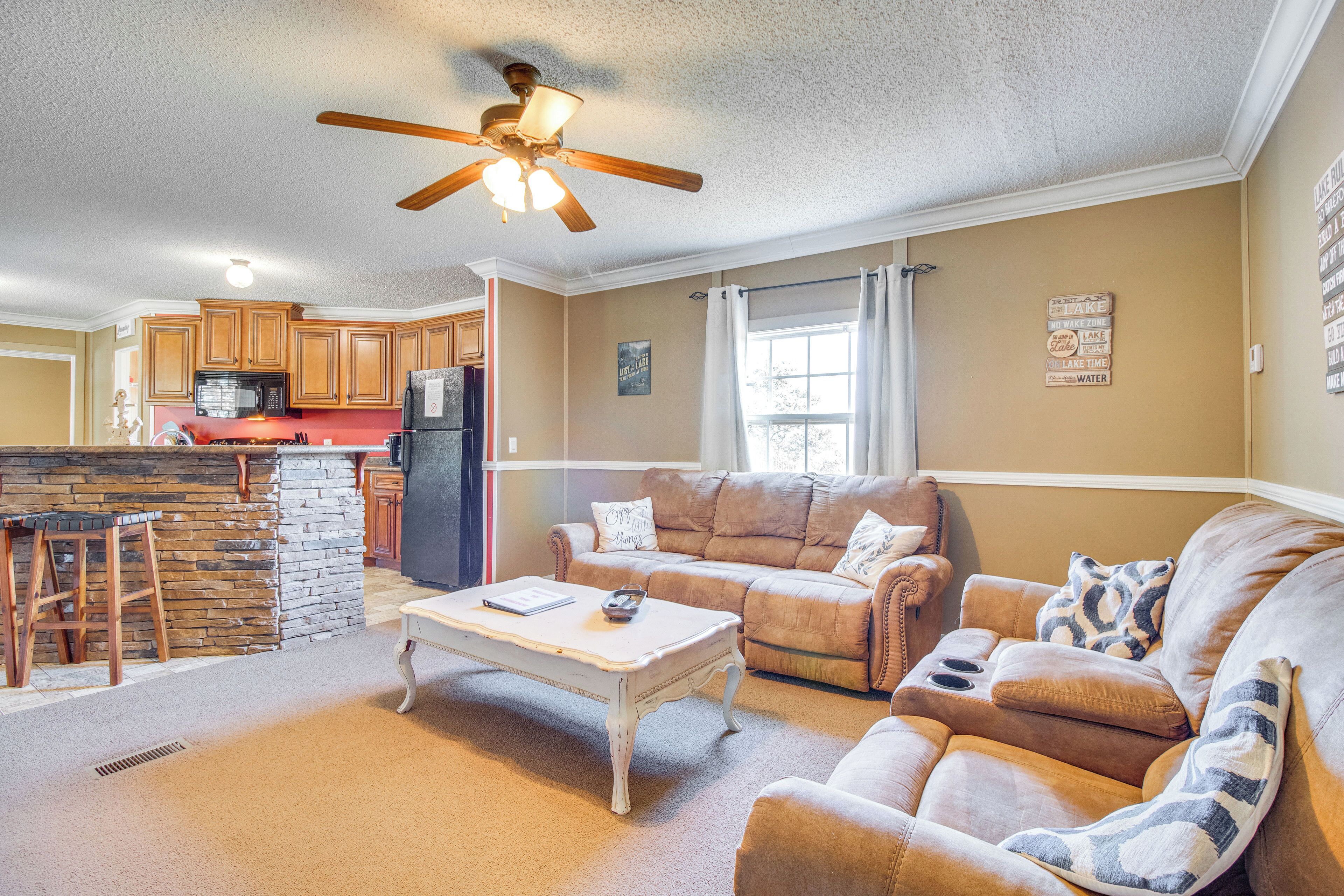 A spacious living area with a sofa set, a coffee table, and a kitchen in the background.