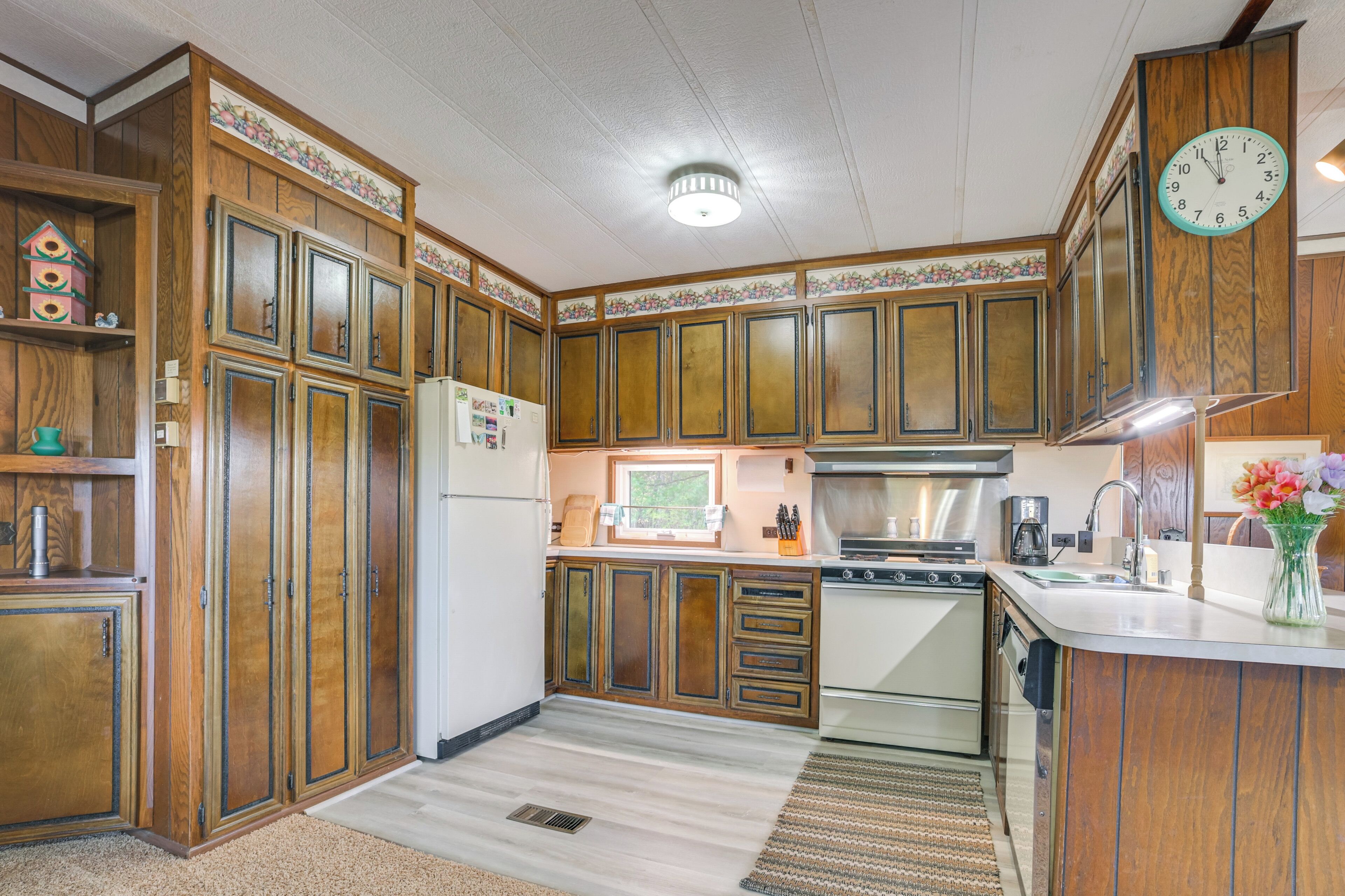 A kitchen with wooden cabinets, a refrigerator, a stove, and a clock on the wall.