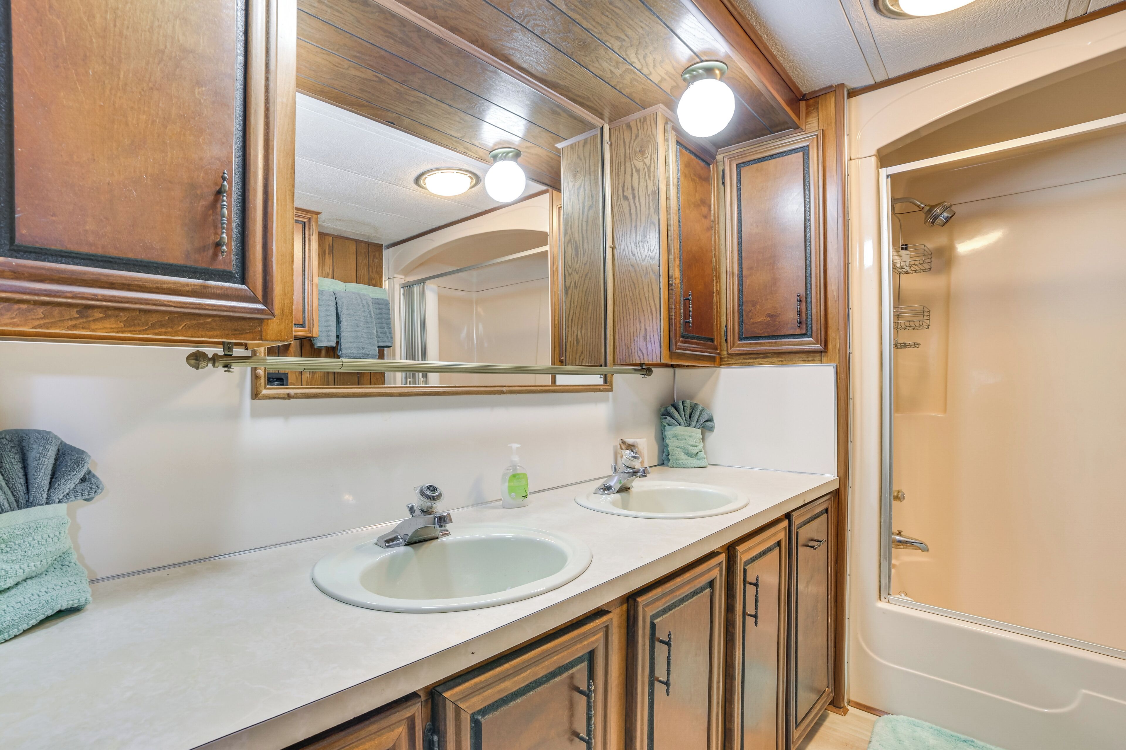 A bathroom with wooden cabinets, two sinks, a large mirror, and a shower.
