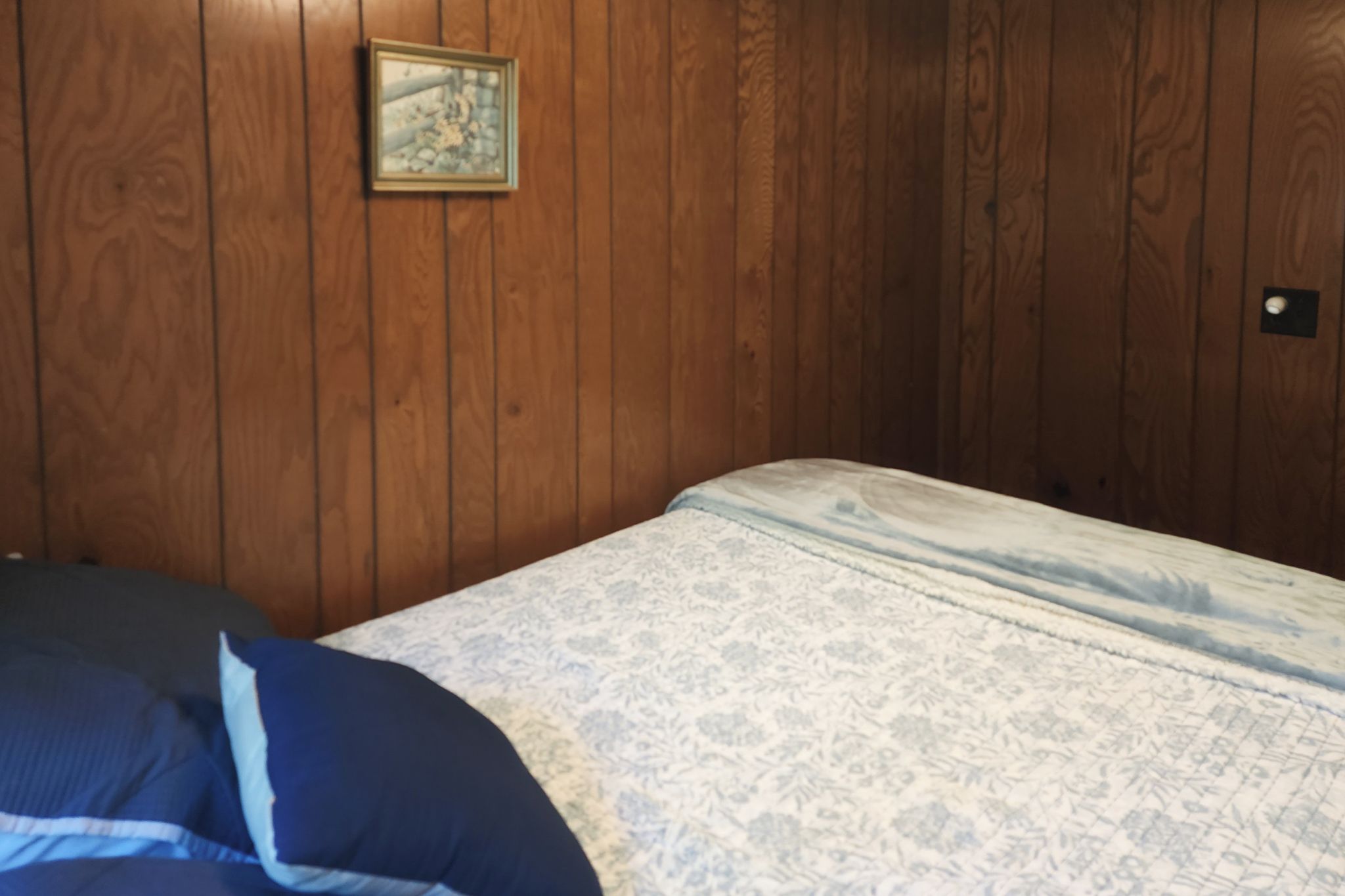 A room with wooden walls, a bed with a patterned bedspread, and a framed picture on the wall.