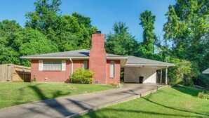 A single-story brick house with a garage, surrounded by a well-maintained lawn and trees.