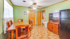 A dining area with a wooden table and chairs, a ceiling fan, and a refrigerator.
