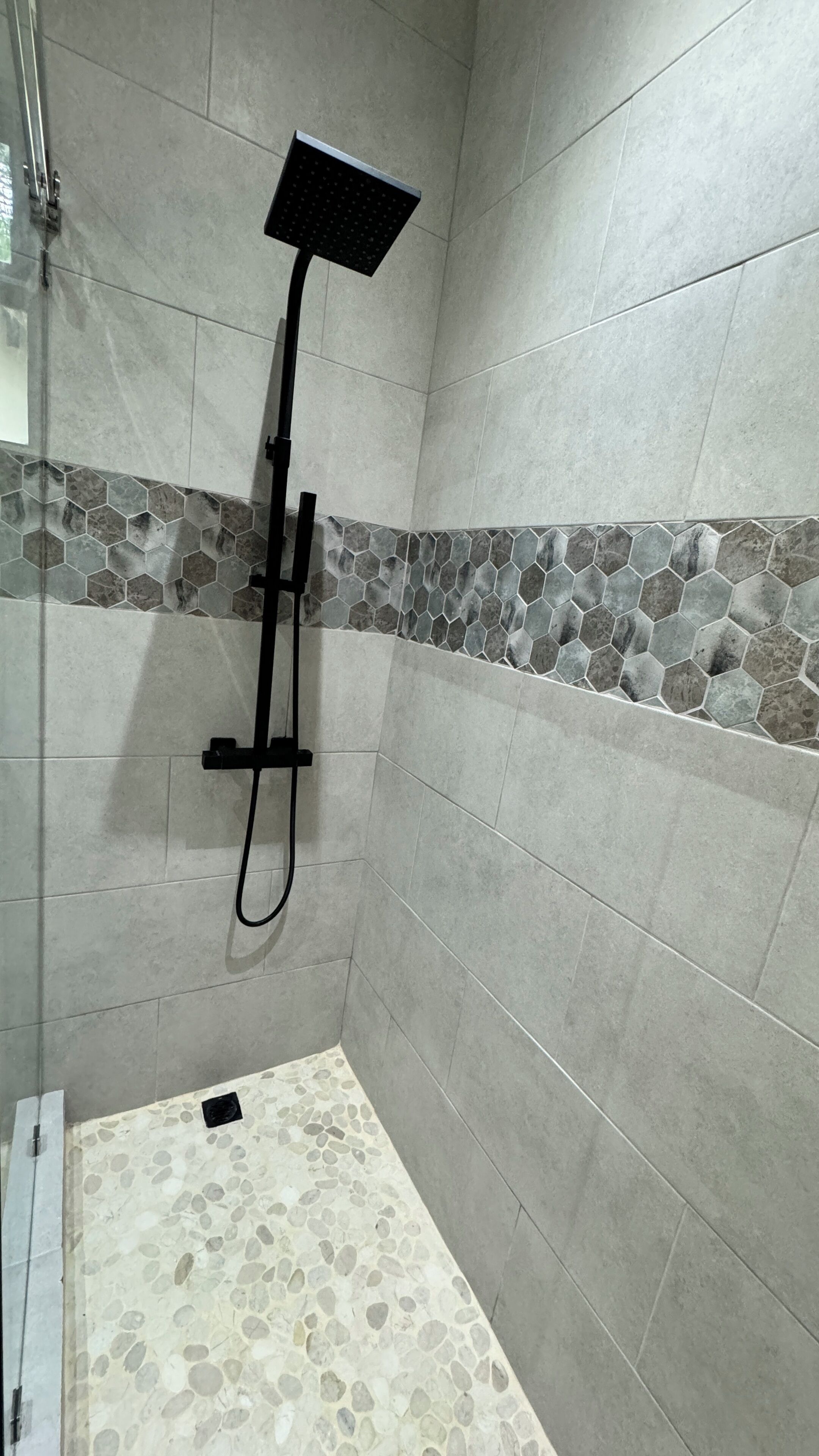 Un área de ducha con pared de azulejos, un borde de azulejos hexagonales y un suelo con diseño de guijarros.