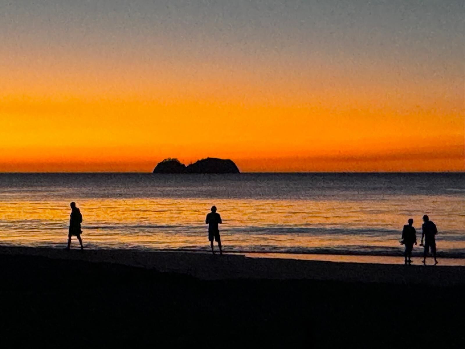 A beach scene with people walking along the shore during sunset.