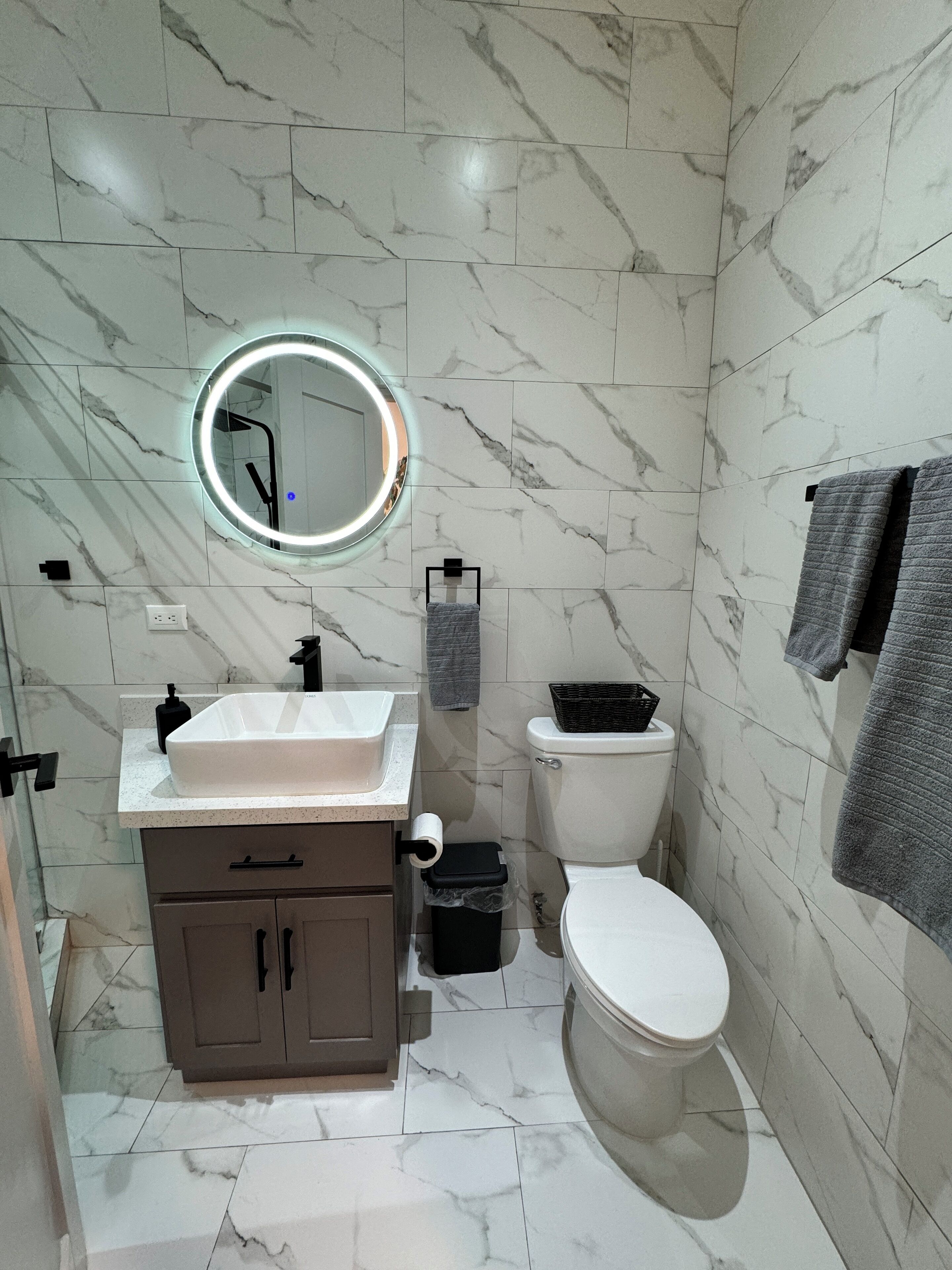A bathroom with a white sink, mirror, toilet, and marble-patterned walls.