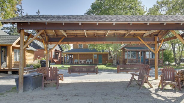 Een overdekt terras met houten stoelen en een bankje, omringd door blokhutten.