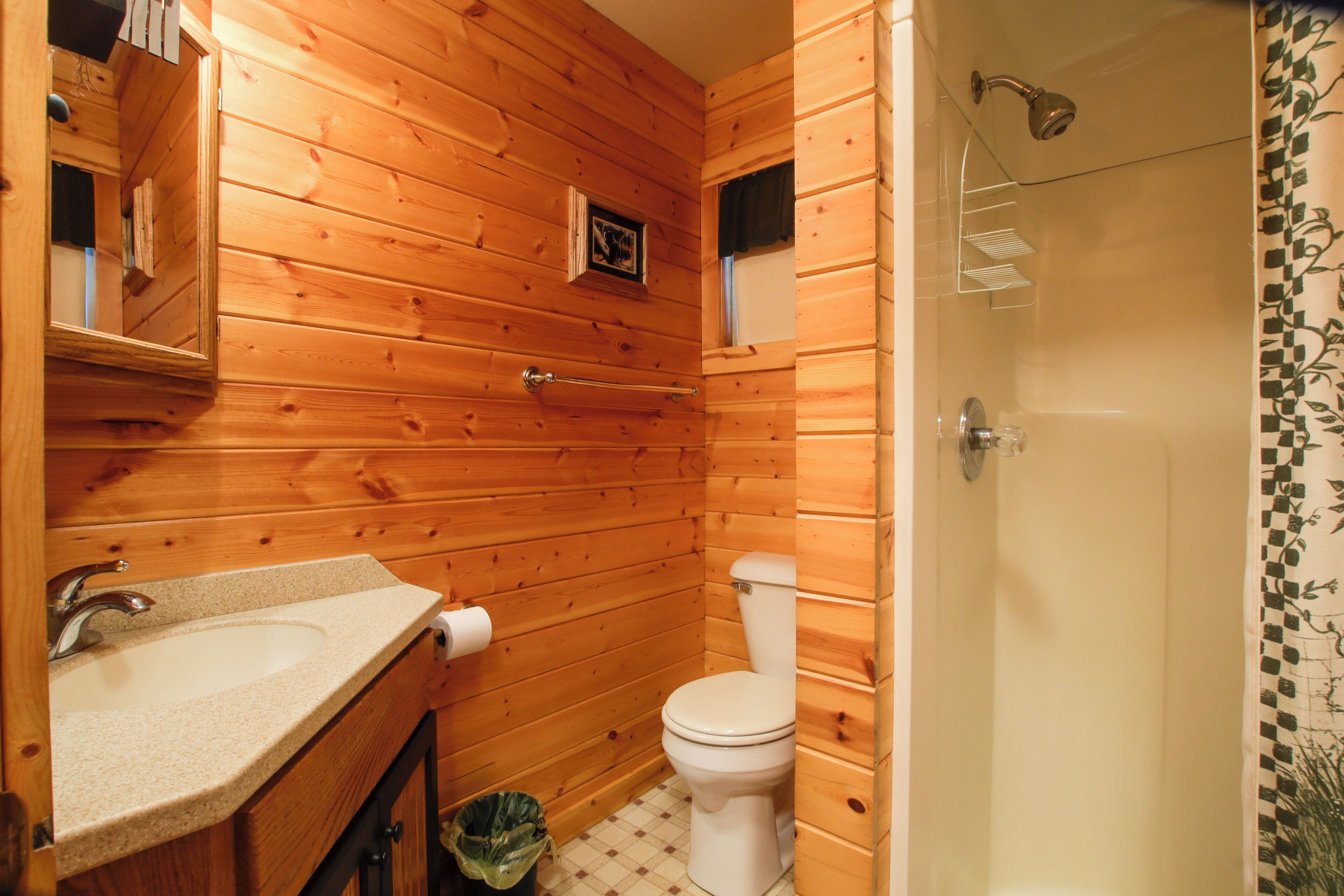 Ein Badezimmer mit Holzwandverkleidung, Waschbecken, Toilette und Dusche.