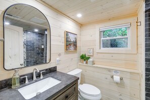 Une salle de bain avec un intérieur en bois, un grand miroir, un lavabo, des toilettes et une fenêtre donnant sur un paysage verdoyant.