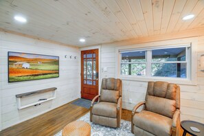 A cozy room with wooden walls, a large window, two leather chairs, a wooden door, and a painting on the wall. - Mountain Haven: Little House on Big Horse Creek (Lansing)