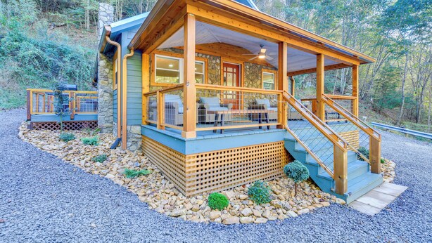Una cabaña con terraza de madera, paredes de piedra y un porche cubierto con mobiliario exterior.