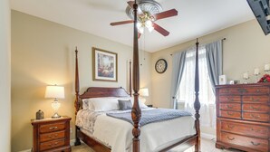Een slaapkamer met een hemelbed, een houten dressoir, een nachtkastje, een plafondventilator en een klok aan de muur.