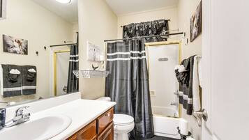 A bathroom with a white sink, vanity, toilet, and bathtub.